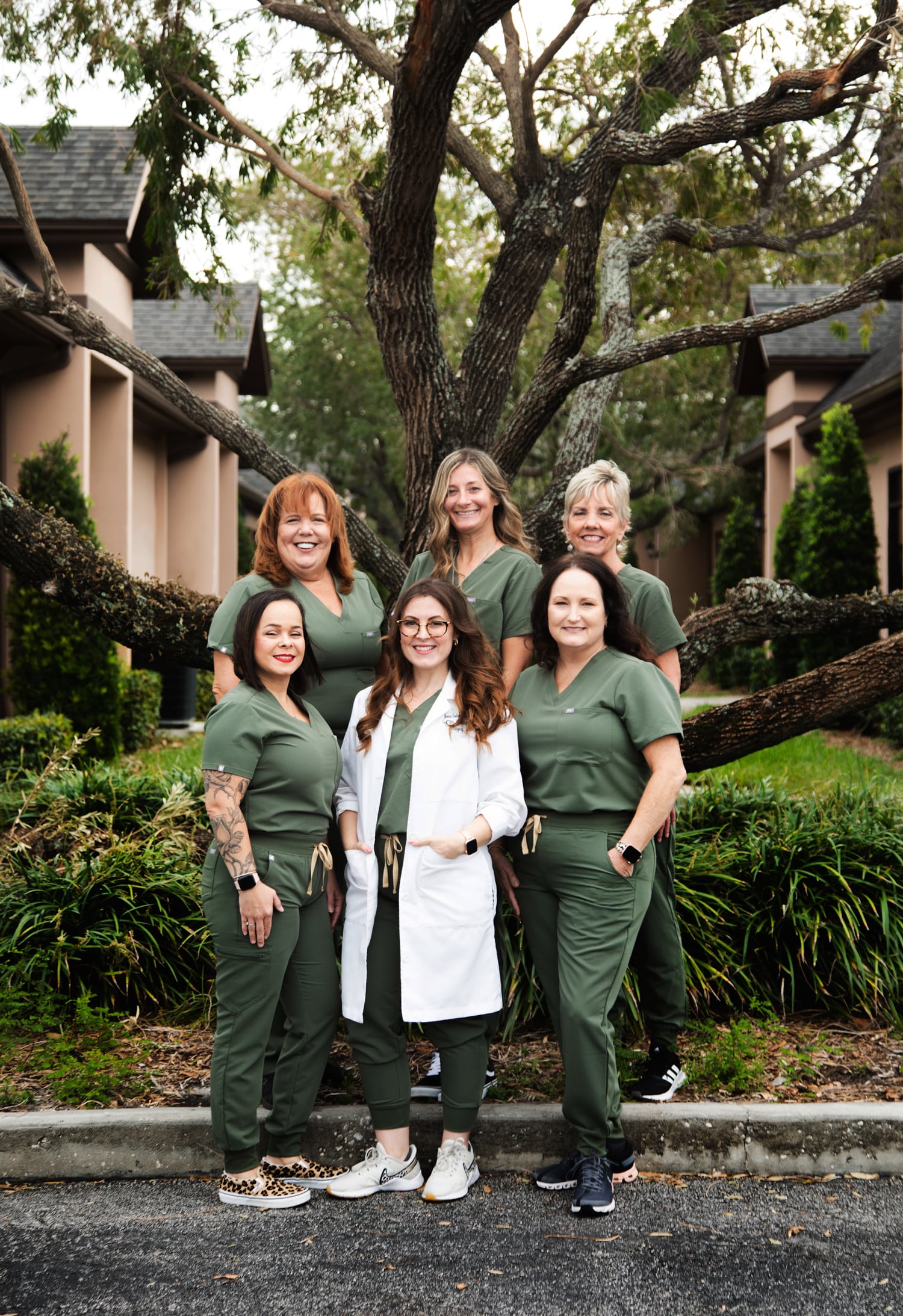 Group of women in green scrubs outdoors, smiling together. mobile